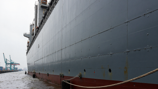 Large cargo ship docked at a modern container port terminal, cranes loading containers under cloudy sky